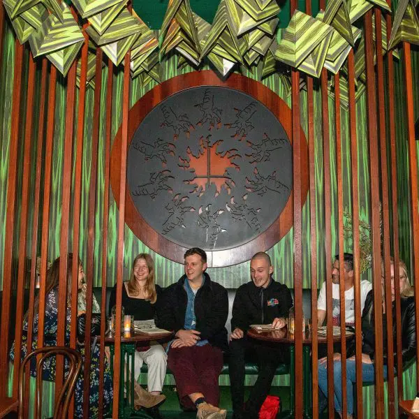 A group of people sitting at a table in a green-themed room with wooden railings and decorative elements on the walls, including a large circular artwork.